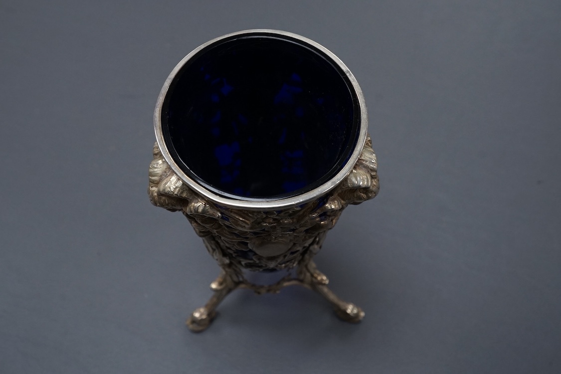 A late Victorian continental pierced silver posy vase, with blue glass liner, decorated with cupids, ram's heads and birds, on tripod supports with hoof feet, import marks for William Moering, London, 1898, height 15.2cm